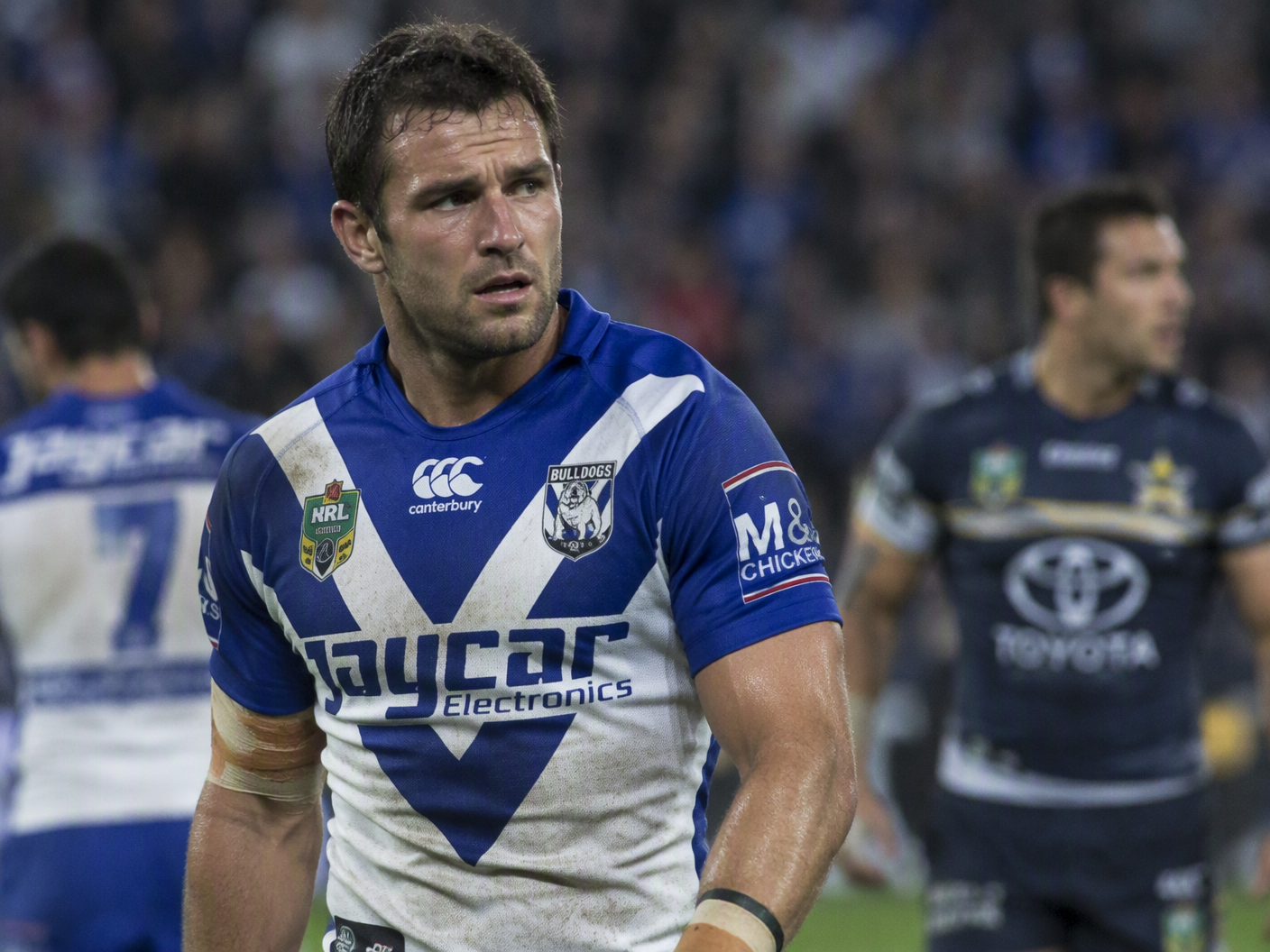 Ryan Tandy wearing Canterbury-Bankstown Bulldogs jersey, captured mid-play on the rugby field under stadium lights in 2010, showing a focused but tense expression amid match action.